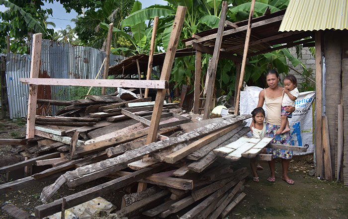 Woman stands with two young children amongst the wreckage of her home in the Philippines