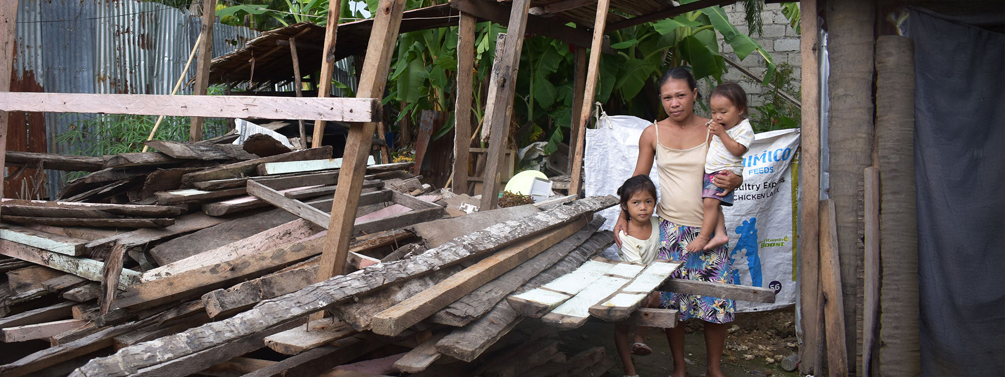 Woman stands with two young children amongst the wreckage of her home in the Philippines