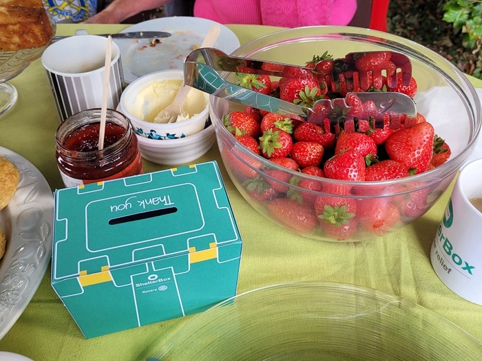 A bowl of strawberries is on a table next to some clotted cream, jam, and a ShelterBox collection box.